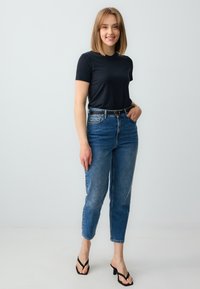 T-shirt nera a maniche corte, jeans a vita alta di colore azzurro chiaro, cintura nera con fibbia rotonda e infradito nere con tacco. Look semplice e casual.