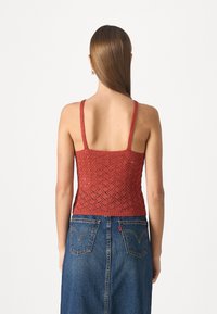Haut court en tricot rouge avec un motif en losanges, des bretelles fines et un design ajusté, associé à une jupe en denim bleu avec des poches arrière.