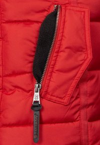 Red puffer jacket section with a black fleece-lined zipper pocket, metallic zipper, and fabric detailing. Stitched and quilted texture evident.