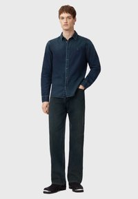 Tmavě modrá džínová košile s designem na knoflíky, doplněná tmavými volnými kalhotami. Obsahuje decentní logo a kontrastní prošívání.