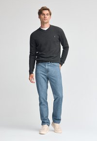 Mörkgrå stickad tröja med rund hals, kombinerad med ljusblå jeans och beige sneakers. Enkel design utan synliga mönster.