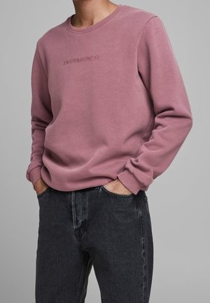 Rosa Sweatshirt mit geripptem Rundhalsausschnitt und Bündchen. Mit geprägt Logo auf der Brust. Getragen mit dunkelgrauen Jeans. Weicher Stofftextur.
