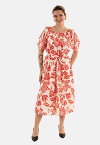 Vestido midi de estampado floral rojo con mangas cortas y abullonadas, y un cinturón a la cintura. Hecho de una tela ligera con una base blanca. Tacones negros complementan el conjunto.