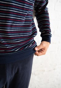 Pull-over rayé bleu marine avec des rayures rouges et blanches, fabriqué en tissu doux. Manches et ourlet côtelés, porté sur un pantalon sombre assorti.