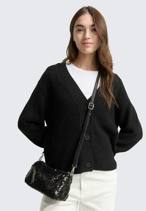 Cardigan nero in maglia con scollatura a V, tessuto a coste e grandi bottoni. Abbinato a una maglietta bianca e una piccola borsa a tracolla nera in paillettes.