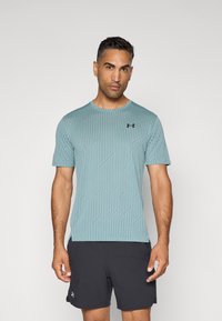 Camiseta atlética de color azul claro con rayas verticales texturizadas y un cuello redondo, que presenta un pequeño logo negro en el lado izquierdo del pecho.