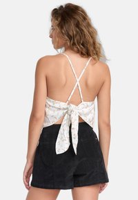 Blomsteret cropped top i hvid, med knyt bagpå, tynde stropper der krydser på ryggen, parret med sorte fløjls-shorts med to baglommer.