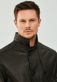 Zwarte leren jas met een hoge kraag, voorzien van een gestructureerde afwerking, dubbele knoopsluiting en een zijzak.