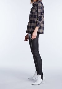 Chemise à carreaux surdimensionnée en bleu marine et beige, associée à un pantalon en cuir noir ajusté et des bottines blanches à bout pointu et petit talon.