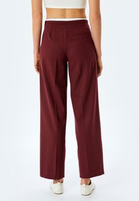 Pantalons larges bordeaux avec une texture lisse, dotés d'une poche arrière, d'un design ajusté et d'une taille classique.