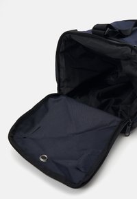 Sac de sport en tissu bleu marine avec fermeture éclair ; l'intérieur est noir avec une texture lisse et un détail de grommet en métal en bas.