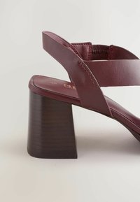 Burgundy leather heeled sandal with a contoured design, wide straps, and a chunky wood-grain heel. Textured surface, minimal stitching detail.
