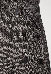 Cappotto con motivo pied de poule in bianco e nero, caratterizzato da un tessuto strutturato, design doppiopetto e grandi bottoni neri.