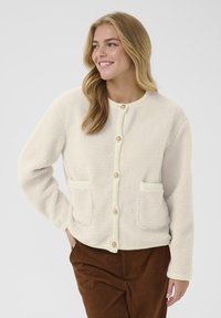 Cremefarbene Fleece-Jacke mit Rundhalsausschnitt, Knopfverschluss und zwei Fronttaschen. Strukturiertem Stoff mit gerippten Akzenten.