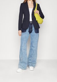 Granatowa dopasowana marynarka, biały top na ramiączkach, szerokie jasnoniebieskie dżinsy z ciemnoniebieskimi łatami oraz mała żółta torebka na ramię. Białe trampki.