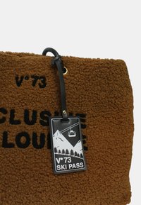 Tessuto marrone texture con testo nero e un tag di pass per la sciata nero che mostra montagne, alberi e una seggiovia.