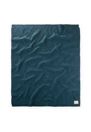Coperta lavorata a maglia di colore verde teal scuro con motivo a rombi e bordi a coste, con una piccola etichetta di tessuto in un angolo.