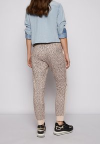 Mönstrade byxor i ljus persika med en svart abstrakt design, med elastiska muddar och sidodetaljer; matchade med svarta sneakers.