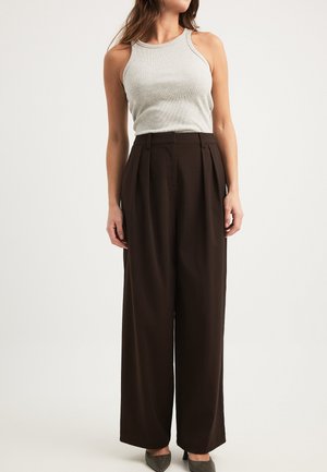 Grå ribbet tanktop parret med højtaljede, brede brune bukser. Bukserne har frontplisseringer og en skræddersyet pasform. Grå stilethæle fuldender looket.