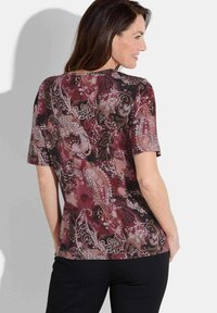 Haut à manches courtes en bordeaux avec un motif cachemire, présentant des motifs floraux complexes dans des teintes de rose, blanc et noir. Texturé en tissu doux.