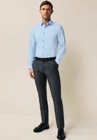 Chemise bleu clair à manches longues, pantalon ajusté gris foncé et chaussures noires ; tissu lisse, coupe structurée et design minimaliste.
