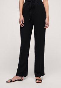 Czarne, wysokie spodnie z elastycznym pasem, prostym krojem nogawek i gładką teksturą. Połączone z czarnymi sandałami z złotym akcentem.