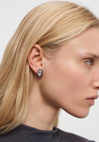 Orecchino a caso d'argento a forma di cuore con finitura lucida, che mostra una superficie liscia e un contorno attorno all'orecchio.