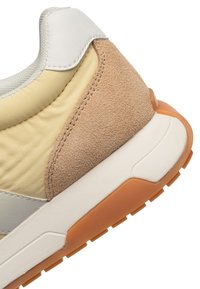 Teniska s bielym koženým golierom, svetložltým textilným zvrškom, hnedými semišovými prvkami, bielou medzipodrážkou a oranžovou gumovou podrážkou.