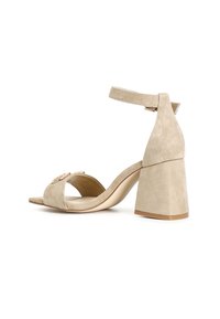 Sandalo con tacco alto in suede beige, con cinturino alla caviglia, design open-toe e tacco a blocco largo. Presenta una fibbia decorativa sul davanti.