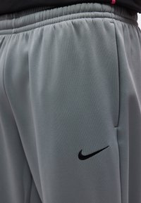 Κοντινό πλάνο γκρι παντελονιών Nike με ελαστική μέση και μαύρο λογότυπο Nike Swoosh στο πάνω μέρος του μηρού.