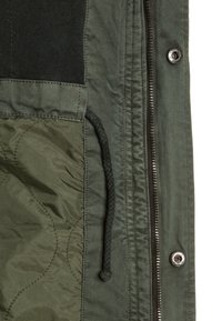 Zielona kurtka z pikowaną podszewką, widocznym zamkiem błyskawicznym, guzikami zatrzaskowymi oraz detalami w postaci sznureczka; wykonana z teksturowanej tkaniny z gładkimi akcentami.