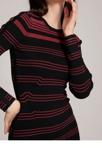 Pull noir à côtes avec des rayures horizontales bordeaux, col rond et manches longues, tissu texturé et coupe ajustée.