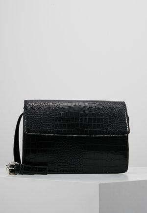 Sac à main rectangulaire noir avec texture crocodile, fermeture à rabat et bandoulière amovible avec boucle argentée, posé sur une surface blanche.