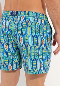 Shorts de bain en tissu bleu avec un motif de formes de feuilles multicolores. Taille élastique avec logo, poches latérales et texture légère.