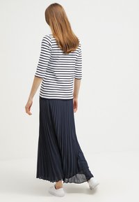 Stribet, trekvartærmet top i hvid og navy, parret med en navy plisseret maxiskirt. Hvide sneakers fuldender outfittet.