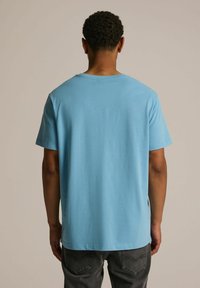 Jasnoniebieska bawełniana koszulka z krótkim rękawem i okrągłym dekoltem, charakteryzująca się gładką fakturą i luźnym krojem, widziana z tyłu.