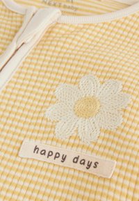 Geltonos ir baltos spalvos pledinis kūdikio aprangos komplektas su baltos spalvos išsiuvinėta ramunėle ir priekyje esančia audinio etikete "happy days".