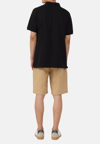 Schwarzes Poloshirt mit lockerer Passform, kurzen Ärmeln und klassischem Kragen, kombiniert mit hellbeigen Shorts und weißen Sneakern.
