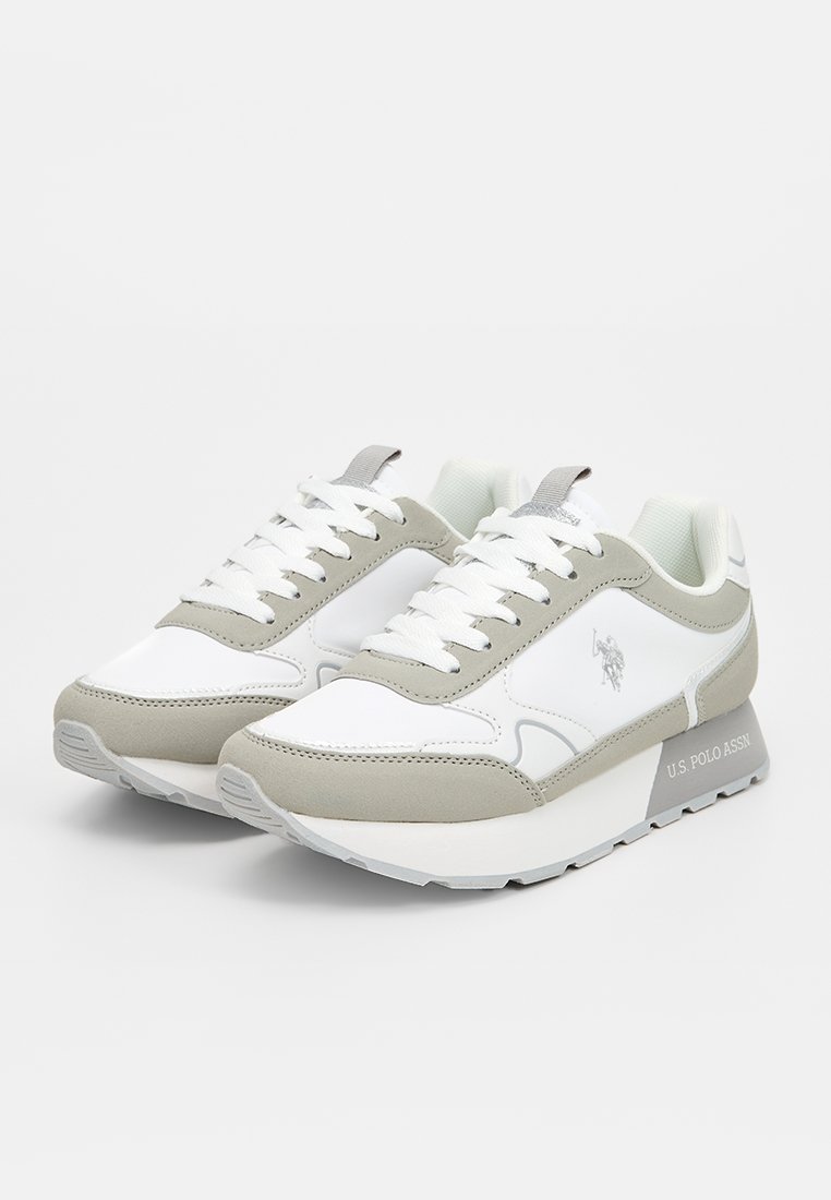 Zapatillas deportivas blancas y grises con cuero texturizado, cuello acolchado y detalles de logo. Presentan cordones planos y una suela de goma ligera.