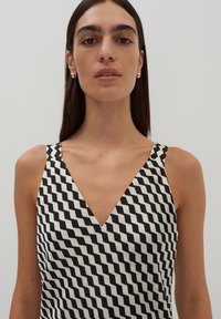 Schwarz-weißes ärmelloses Kleid mit V-Ausschnitt, das ein geometrisches Zickzackmuster aufweist und aus einem glatten Stoff gefertigt ist.