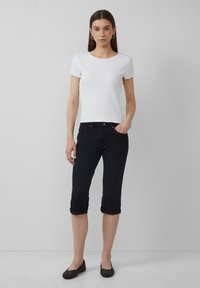 Biała, prążkowana bluzka z krótkim rękawem z falbaniastymi krawędziami, zestawiona z czarnymi, ściśniętymi spodniami do kostek i czarnymi, teksturowanymi balerinami.