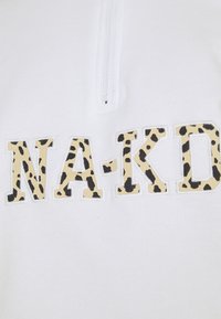 Haut blanc avec un col zippé à mi-hauteur ; présente "NA-KD" en lettres gras, orné d'un motif léopard beige et noir.