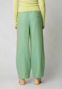 Pantaloni larghi verde in tessuto texturizzato, dotati di due tasche posteriori e un piccolo dettaglio con logo blu.