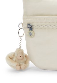 Beige nylon taske med en lynlåslomme og en gummiecharm nøglehank formet som en fluffy beige abe med et simpelt ansigtsdesign.