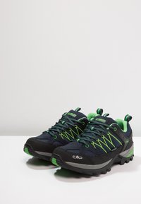 Ciemnoniebieskie buty trekkingowe z zielonymi akcentami, charakteryzujące się teksturowaną cholewką, wyściełanym kołnierzem oraz wytrzymałą czarną gumową podeszwą zapewniającą przyczepność.