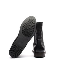 Stivali alla caviglia in pelle nera con tomaia texturizzata, punta rotonda e suola in gomma spessa e decorata per una migliore presa. Design classico, accenti minimi.