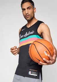 Tricou de baschet negru cu inscripția „San Antonio” și dungi multicolore (turcoaz, roz, portocaliu) pe piept. Jucătorul ține un balon de baschet portocaliu.
