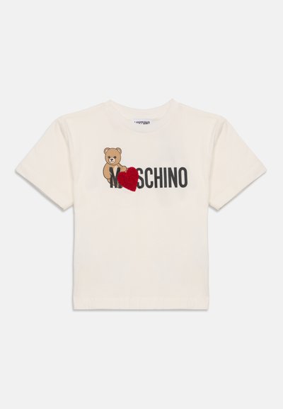 Кремаво късо с ръкав тениска с изображение на меченце и черен "Moschino" текст, с червено текстурирано сърце, покриващо част от текста.