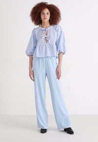 Μπλουζάκι σε μπλε και άσπρο καρώ σχέδιο με φουσκωτά μανίκια, μεσάτο, συνδυασμένο με ανοιχτό μπλε παντελόνι σε φαρδιά γραμμή και μαύρες μπότες με τακούνι.