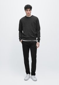 Tmavě šedý svetr, černé kalhoty a bílé tenisky. Jednoduchý design s kulatým výstřihem a žebrovanými manžetami. Hladká textura, přiléhavý střih.